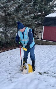 A Poopy Monster Technician Scooping Poop in a yard next to a shed.